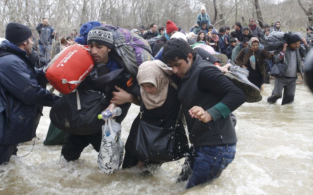 Мигранты идут вброд через реку рядом с греко-македонской границей, к западу от села Идоменей, Греция. 14 марта сотни мигрантов прорвались на территорию Македонии. / © Reuters