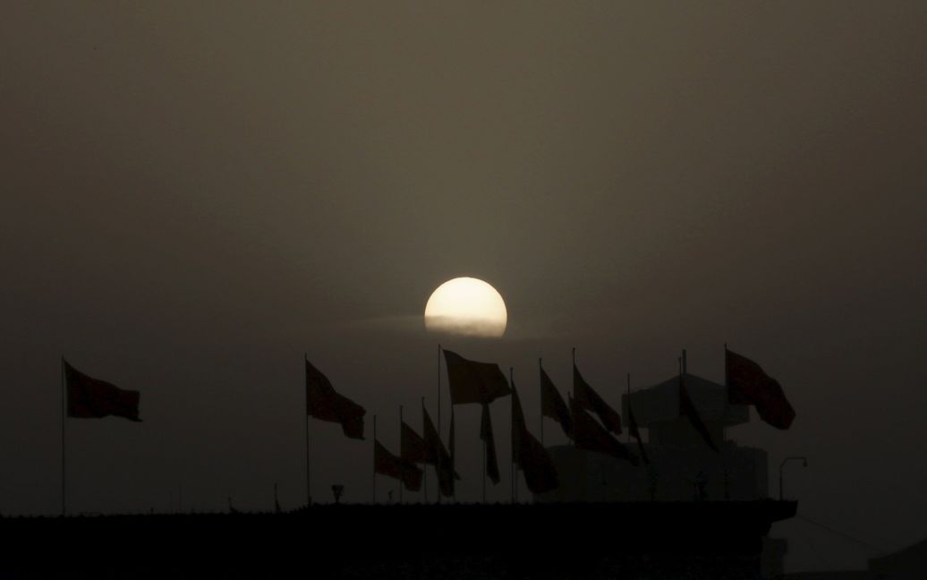 Солнце поднимается над красными флагами на крыше флаттера Национального музея на площади Тяньаньмэнь перед открытием сессии Всекитайского собрания народных представителей в Пекине, Китай. / © Reuters
