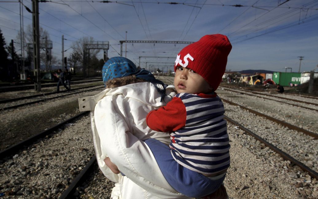 Мигрант несет ребенка по дороге к импровизированному лагерю для беженцев на греко-македонской границе, недалеко от села Идоменей, Греция. / © Reuters
