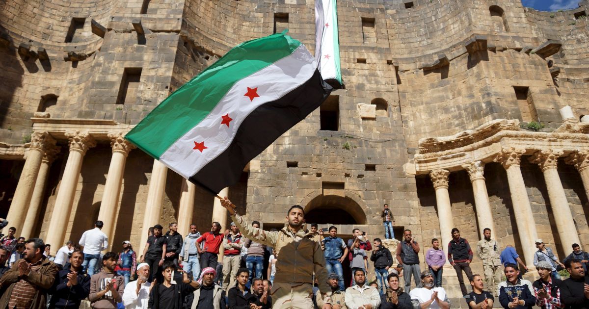 Протестующий держит флаг сирийской оппозиции во время антиправительственной акции протеста внутри римского амфитеатра второго века в историческом сирийском южном городе Босра аль-Шам. / © Reuters
