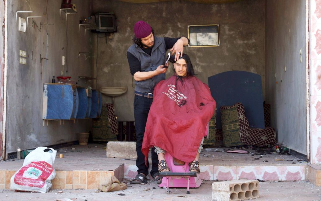 Парикмахер срезает волосы клиента за пределами своего поврежденного салона в городе аль-Гарбия в провинции Дераа, Сирия, который находится под контролем повстанцев. / © Reuters
