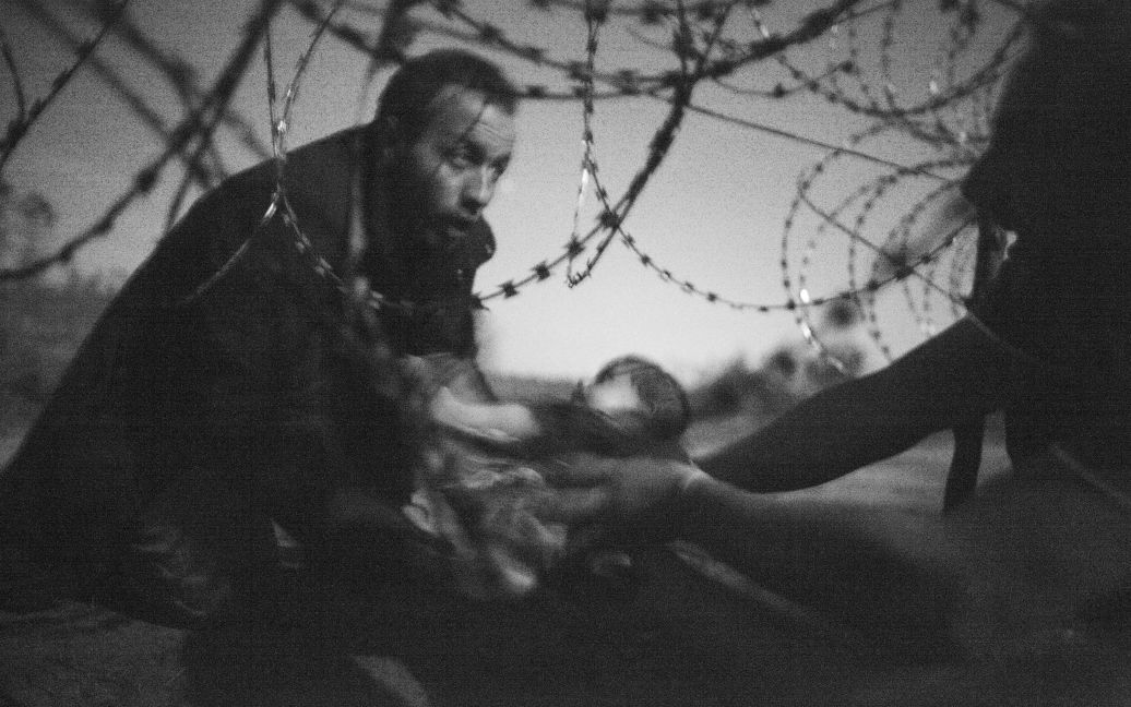 Фото победителя Уоррена Ричардсона &ldquo;Надежда на новую жизнь&rdquo;. Изображен сирийский беженец, который передает маленького ребенка сквозь колючую проволоку, пытаясь пересечь венгерско-сербскую границу. / © Reuters