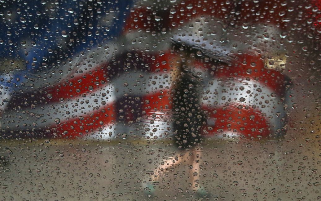 Женщина ходит с зонтиком во время дождя на фоне флага США, нарисованном на здании в Манхэттене в Нью-Йорке. / © Reuters