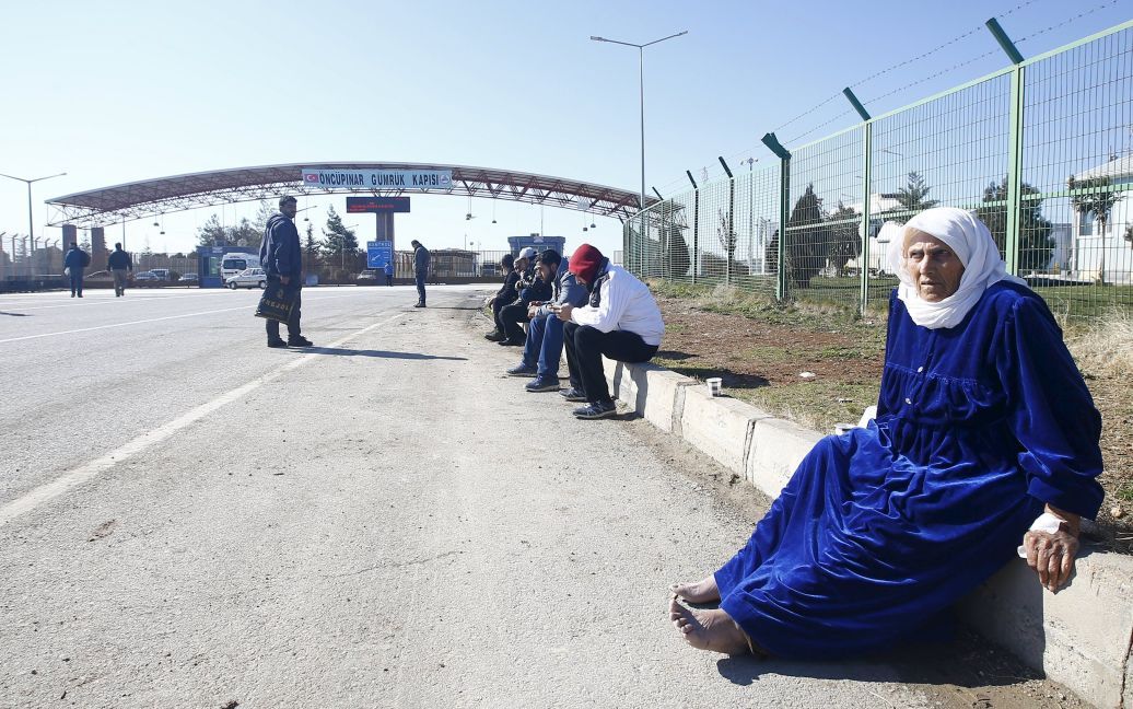 Люди сидят на тротуаре, на пересечении границы с Турцией, в юго-восточном городе Килис. / © Reuters