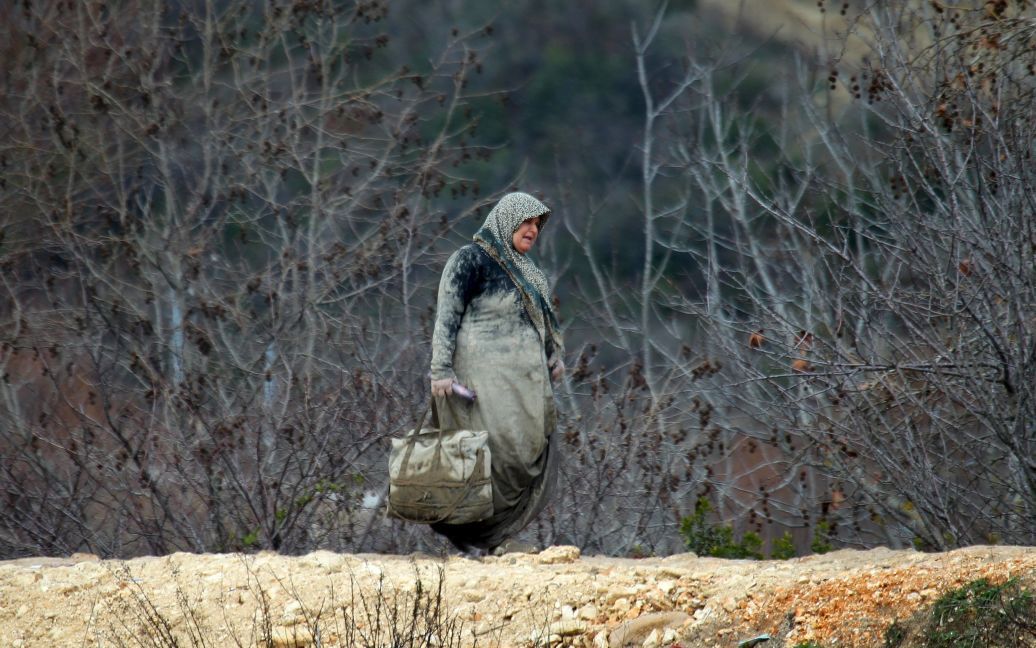 Сирийская женщина несет свои вещи в городе Хирбет Аль-Джоз, ожидая разрешения пересечь границу с Турцией. / © Reuters