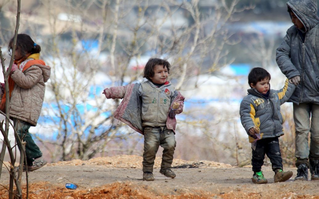 Дети-беженцы, все в грязи, ждут разрешения пересечь границу в Турцию со своими семьями в городе Хирбет Аль-Джоз. / © Reuters