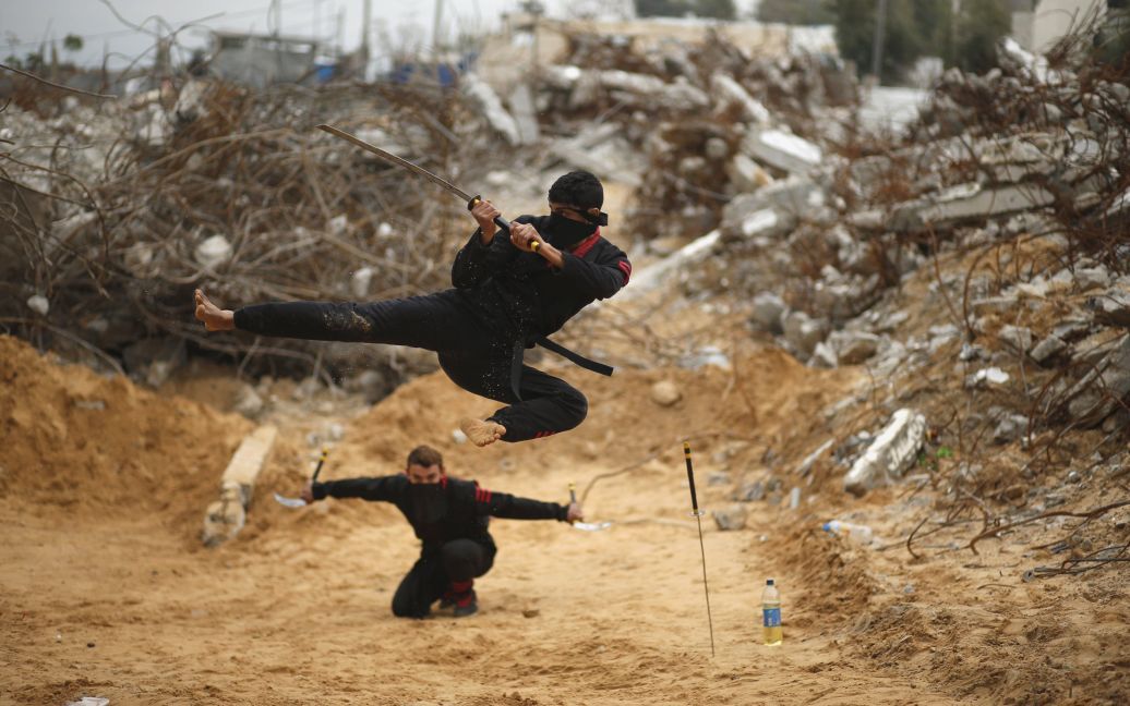 Палестинские парни прыгают с мечами, демонстрируя свои навыки ниндзя среди  руин зданий, которые были разрушены в 2014 году во время войны в северной части сектора Газы. / © Reuters