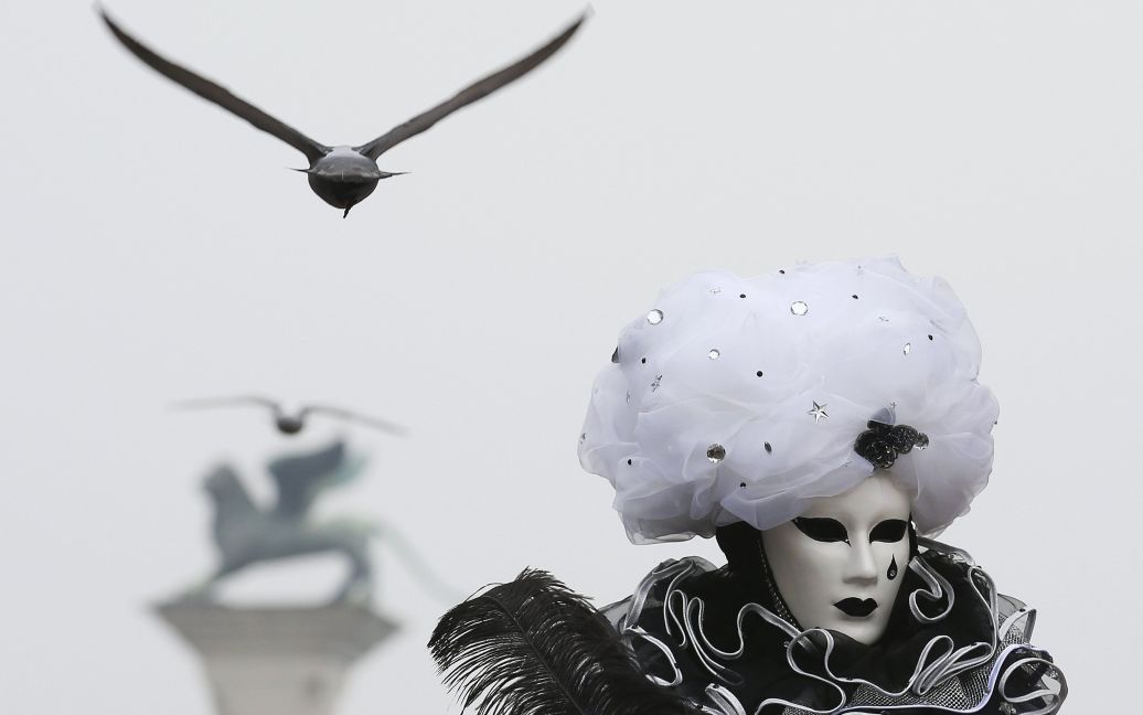 Участник Венецианского карнавала позирует для фото, а позади него летит птица. / © Reuters