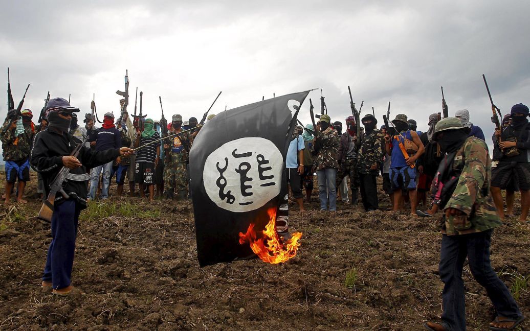 Христианская вооруженная группа самообороны, которая называет себя &laquo;Защитники Красного Бога", поджигает флаг "Исламского государства" в Минданао на юге Филиппин. Около 300 ополченцев поклялись защищать свои земли и семьи от зверств местных боевиков-исламистов из группировки Моро. / © Reuters