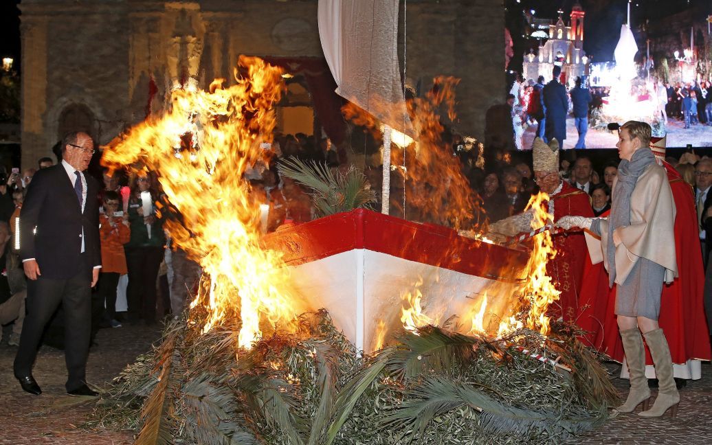 Принц Монако Альберт II и его супруга принцесса Шарлин держат факел, чтобы сжечь маленькую рыбацкую лодку во время традиционных торжеств возле церкви Сент-Девот. / © Reuters