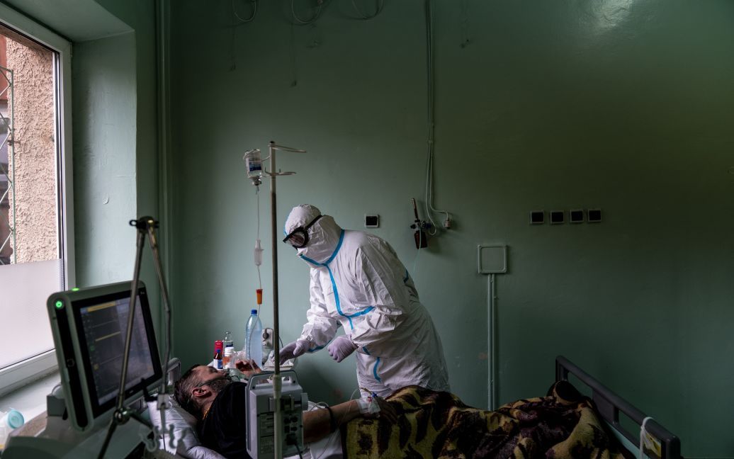 На этом фото, сделанном в понедельник, 4 мая 2020 года, глава отделения интенсивной терапии Константин Дроник в специальном защитном костюме помогает пациенту с кислородной маской в Черновицкой областной больнице / © Associated Press