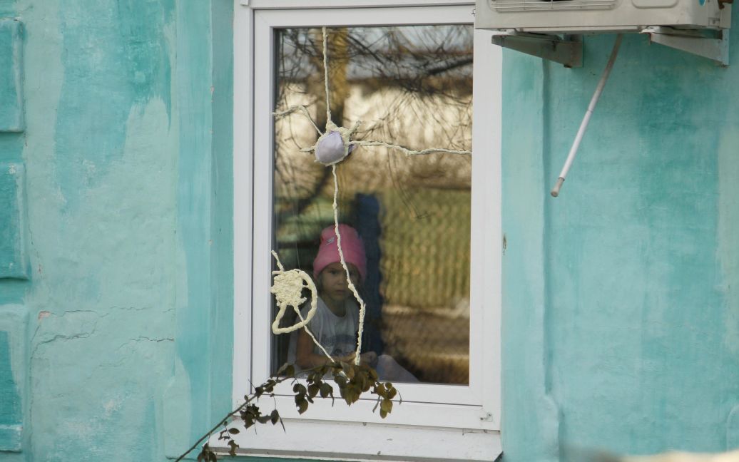 Маленька місцева жителька виглядає на вулицю з потрісканого вікна. / © Reuters