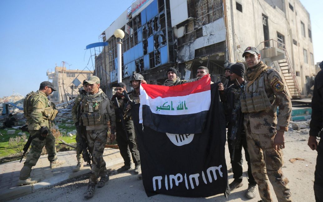 Бійці іракських сил безпеки тримають прапор Іраку над перевернутим догори низом прапором &ldquo;Ісламської держави&rdquo; поблизу урядового комплексу у місті Рамаді. Іракські військові звільнили урядові будівлі у Рамаді від бойовиків ІДІЛ, але ісламісти все ще залишаються в місті. / © Reuters