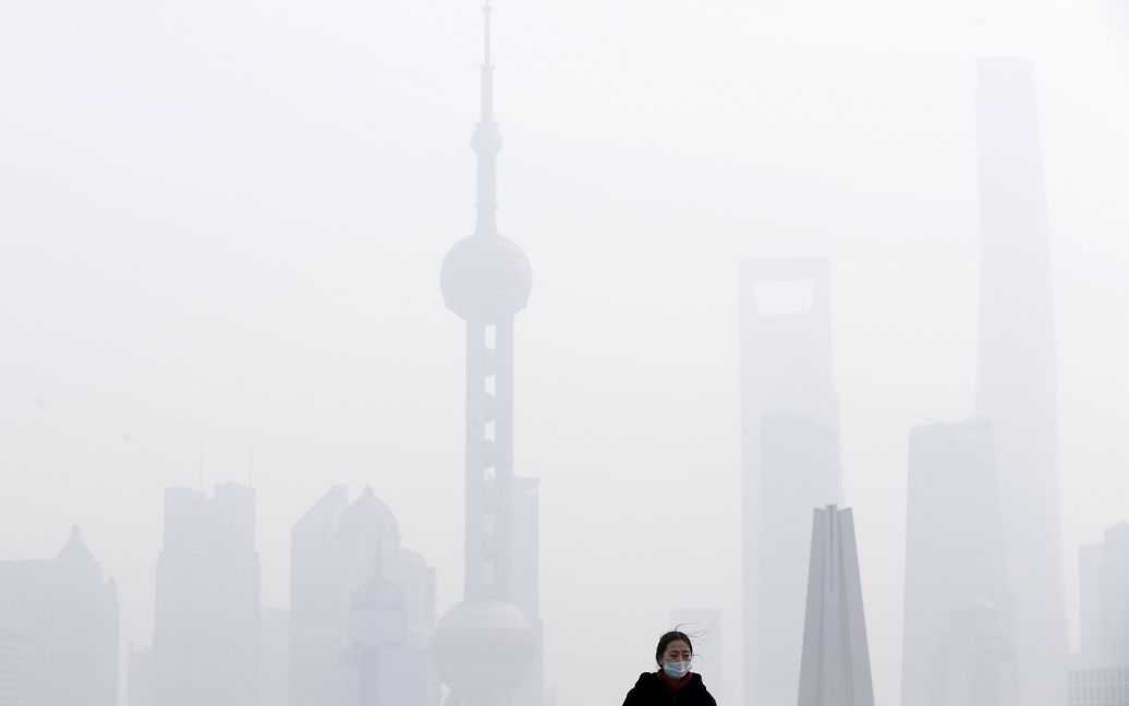Жінка в масці стоїть на мосту перед фінансовим районом Пудун на тлі важкого смогу в Шанхаї, Китай. / © Reuters