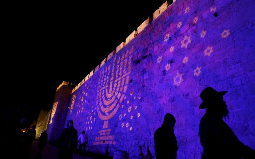 Люди проходят мимо изображением меноры, которая проецируется на стену, окружающую Старый город Иерусалима. Менора - еврейское название для светильника, который используются во время праздника Хануки. / © Reuters