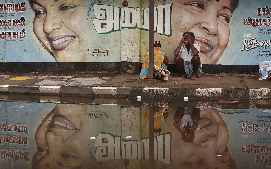 Постраждала від повені пара сидить по затопленій дорозі під зображенням головного міністра південного індійського штату Таміл Наду, в Ченнаї, Індія. Внаслідок руйнівної повені у штаті загинули щонайменше 188 людей. / © Reuters