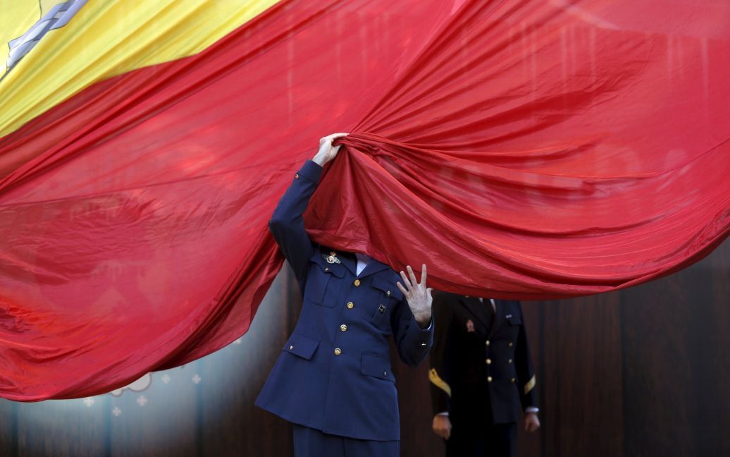 Військовослужбовець Іспанських Збройних Сил прибирає з обличчя гігантський прапор Іспанії, коли допомагає підняти його під час урочистої церемонії з нагоди 37-ї річниці прийняття конституції країни. / © Reuters