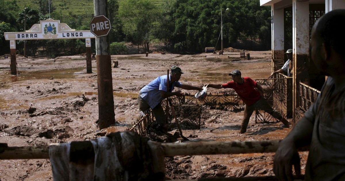 Чоловіки витягають сумку з будинку, затопленому брудом після прориву греблі. Число загиблих від прориву двох гребель, які стримували відходи виробництва,  наразі невідомо, але близько 23 людей залишаються зниклими безвісти. / © Reuters