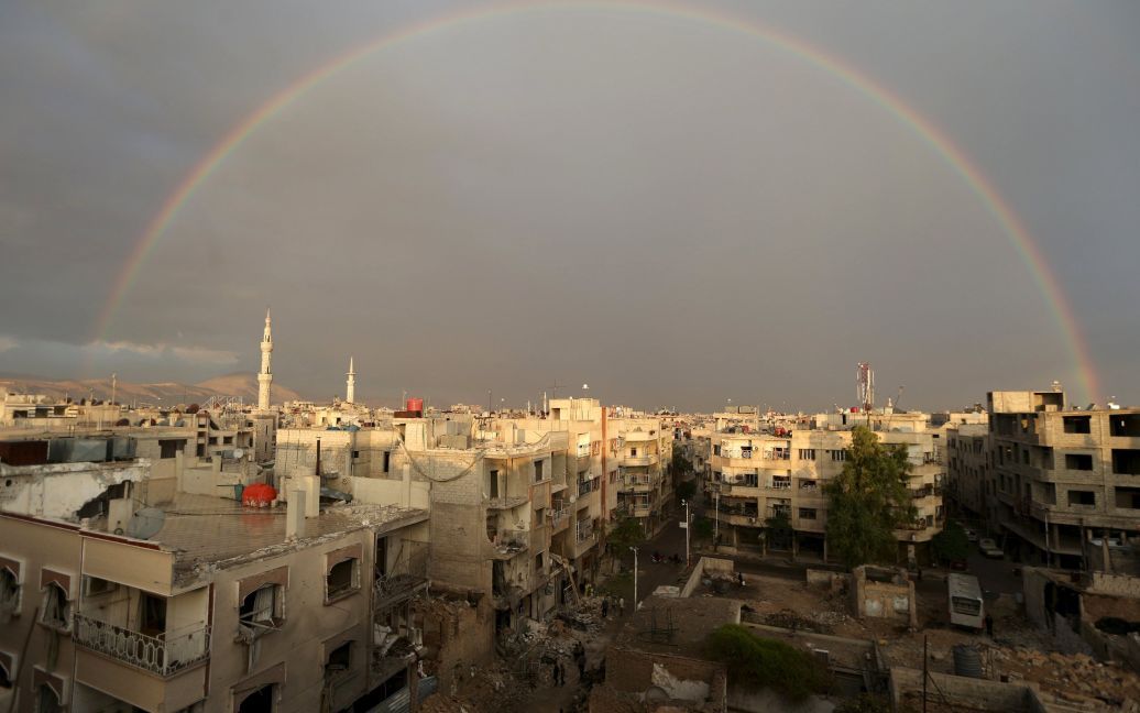 Радуга выглянула над жителями сирийского города Дума, которые осматривают разрушения от бомбардировок главного полевого госпиталя со стороны сил, лояльных к Башару Асаду. / © Reuters