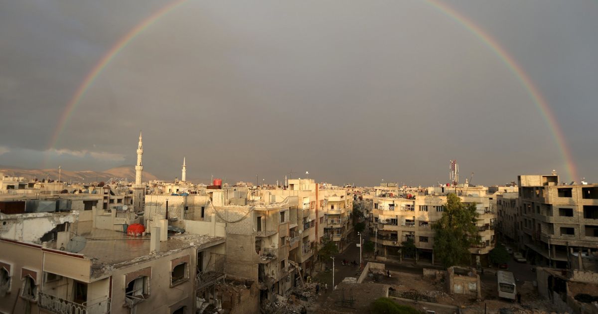 Радуга выглянула над жителями сирийского города Дума, которые осматривают разрушения от бомбардировок главного полевого госпиталя со стороны сил, лояльных к Башару Асаду. / © Reuters