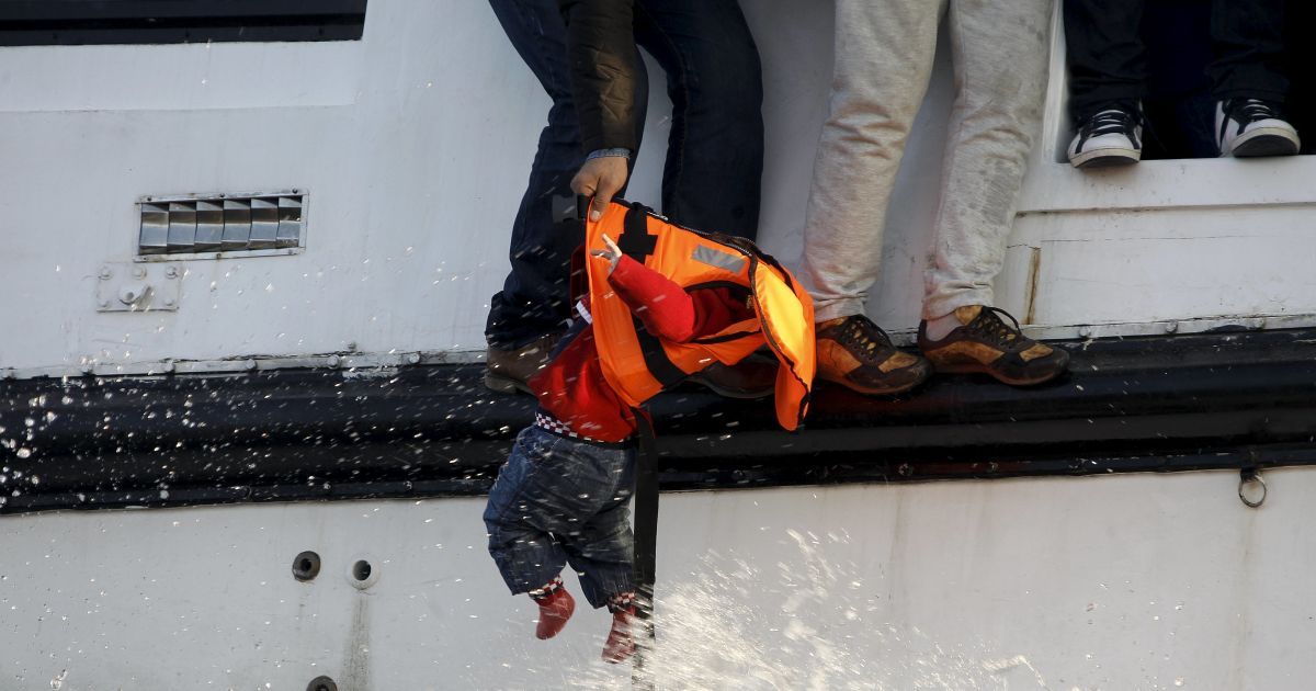 Біженець готується віддати малюка волонтерам-рятувальникам з  наполовину затонулого катамарана, яке несе близько 150 біженців до грецького острова Лесбос. / © Reuters