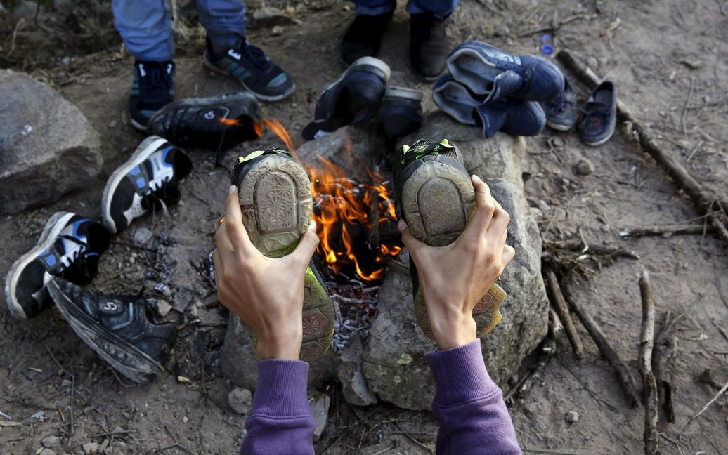 Афганский мальчик сушит ботинки на огне около временного лагеря беженцев на греческом острове Лесбос. Тысячи беженцев, которые бегут от войны в Сирии, Афганистане и Ираке, ежедневно пытаются пересечь Эгейское море со стороны Турции. В этом году в Европу по морю добрались почти 400 000 мигрантов. / © Reuters