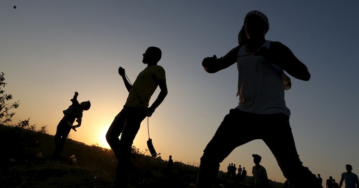 Палестинские демонстранты бросают камни в израильских военных во время столкновений в районе границы между Израилем и центральным сектором Газа. По меньшей мере 40 палестинцев и семь израильтян умерли в столкновениях, которые продолжаются более двух недель. Беспорядки были частично вызваны гневом палестинцев из-за закрытия доступа к мечети Аль-Акса в Иерусалиме. / © Reuters