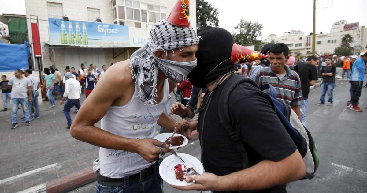 Палестинские демонстранты едят торт, празднуя день рождения товарища во время столкновений с израильскими войсками в районе еврейского поселения Бейт-Эль, недалеко от города Рамалла на Западном берегу Иордана. Палестинские группировки призвали к массовым митингам против Израиля в оккупированном Западном берегу и в Восточном Иерусалиме в "день гнева" в пятницу, 23 октября. / © Reuters
