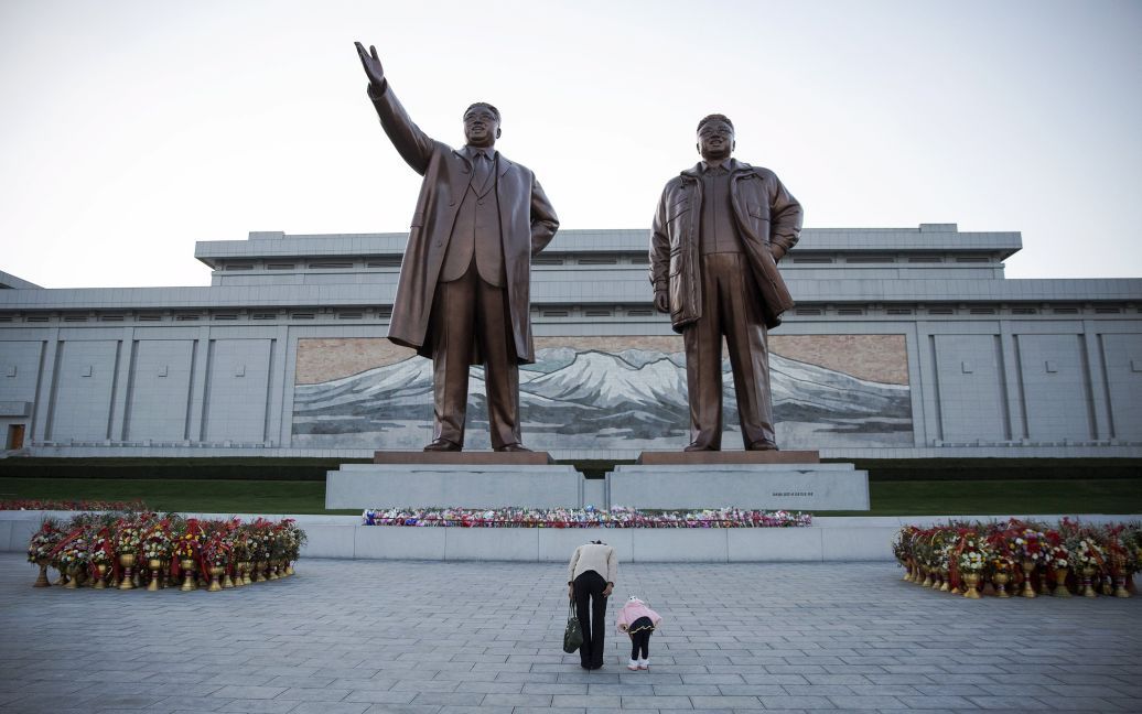 Женщина и ее дочь преклоняются перед статуями основателя Северной Кореи Ким Ир Сена и покойного лидера страны Ким Чен Ира в Пхеньяне. КНДР отметила 70-летие своей правящей Трудовой партии масштабным военным парадом. / © Reuters
