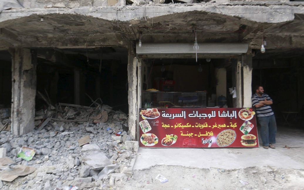 Торговец стоит возле своего киоска по продаже фаст-фуда на фоне руин в Алеппо, Сирия. С 2011 года в стране происходит гражданская война, которая унесла жизни более 220 000 человек. / © Reuters