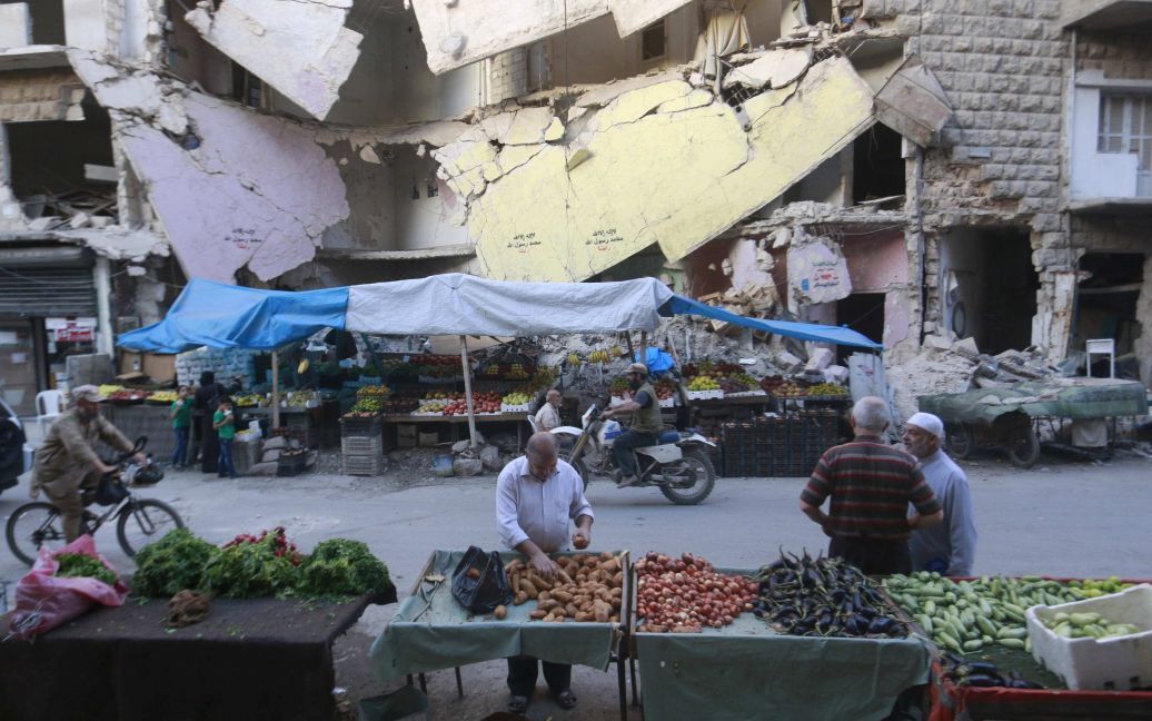 Магазин для овощей и фруктов на фоне перед поврежденных зданий в Бустан аль-Касре, окрестности Алеппо, Сирия. В стране уже более четырех лет продолжается гражданская война, которая унесла жизни более 220 000 человек. / © Reuters
