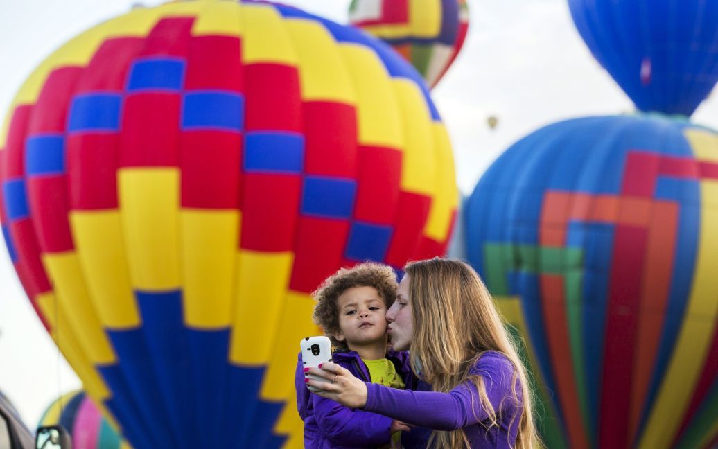 Женщина и ее ребенок фотографируются на фоне воздушных шаров во время фестиваля Albuquerque International Balloon Fiesta в городе Альбукерке (Нью-Мексико, США). / © Reuters