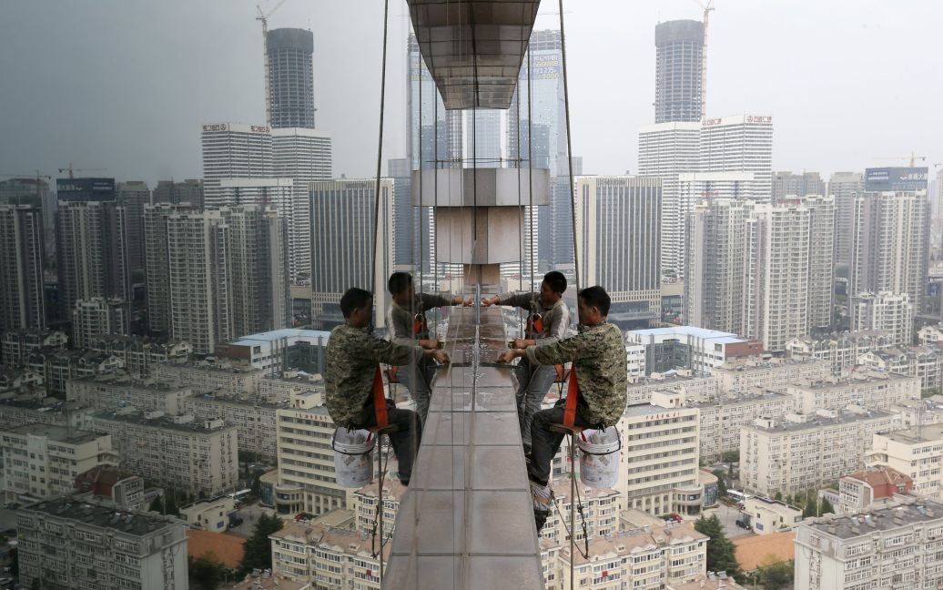 Рабочие моют окна на 30 этаже бизнес-здания в городе Циндао, провинция Шаньдун, Китай. / © Reuters
