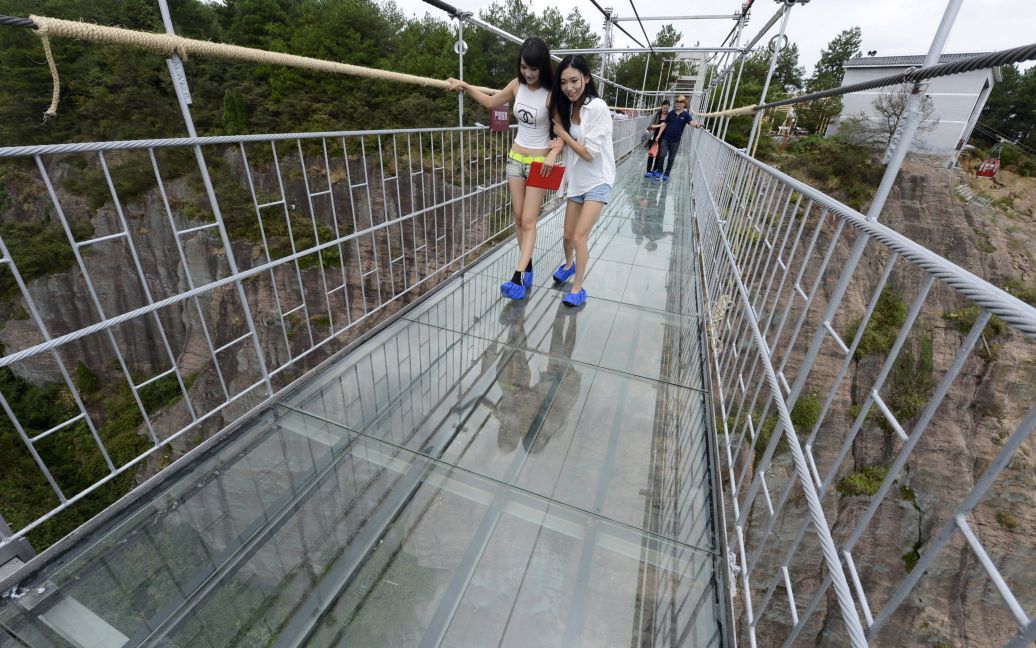Туристы смотрят под ноги, когда ходят по стеклянному подвесному мосту в Национальном парке в провинции Хунань, Китай. 300-метровый стеклянный мост, который впервые открылся для туристов в четверг, висит над каньоном глубиной 180 метров. / © Reuters