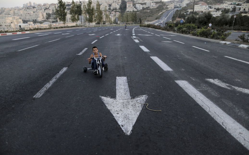 Мальчик ездит на трехколесном велосипеде на пустой улице во время еврейского праздника Йом Кипур. Этот праздник является одним из священных еврейских праздников, когда евреи искупают грехи прошлого года. В Израиле на 25 часов вводится ограничение на работу транспорта. / © Reuters