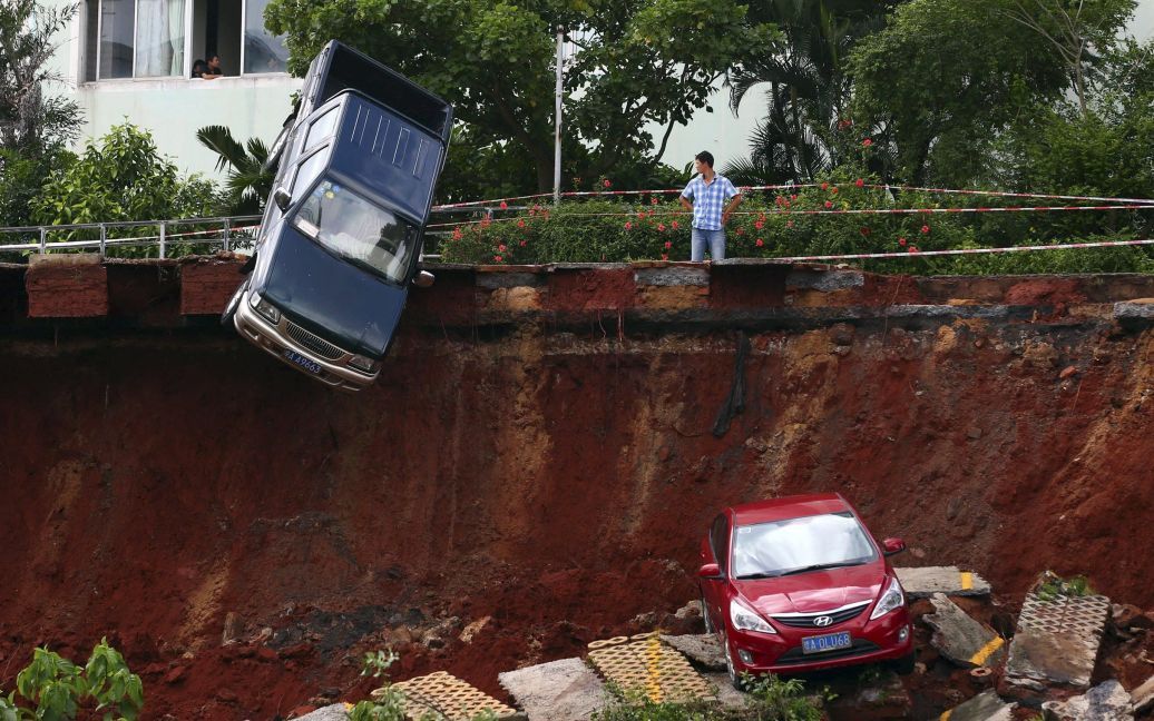 Человек смотрит на автомобиль, который застрял над ямой, образовавшейся из-за проливных дождей в китайском городе Хайкоу, провинция Хайнань. Информации о жертвах в результате стихийного бедствия нет. / © Reuters