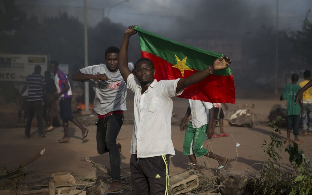 Демонстранты, которые выступают против государственного переворота, держат флаг Буркина-Фасо. Лидеры переворота объявили в пятницу, что освободили исполняющего обязанности президента страны, и двух членов правительства, которых удерживала президентская охрана. Протестовать против военного переворота вышли тысячи жителей Буркина-Фасо, между демонстрантами и мятежниками вспыхивают вооруженные столкновения. / © Reuters