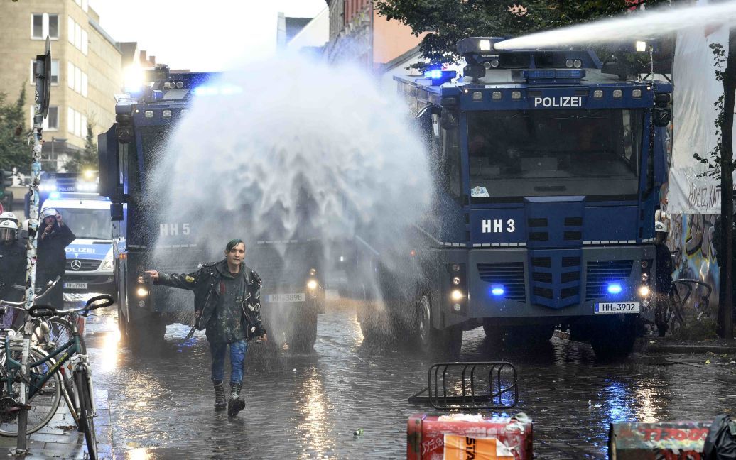 Леворадикальный протестующий идет перед водометом полиции в немецком Гамбурге. 12 сентября более 10 тысяч людей вышли против запланированной на этот день демонстрации неонацистов. Между правыми и левыми радикалами возникли столкновения, в которые вынуждена была вмешаться полиция. / © Reuters