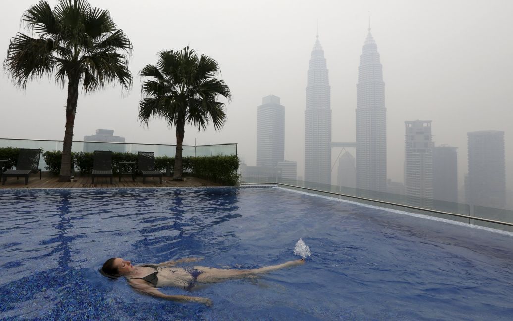 Женщина плавает в бассейне на крыше перед небоскребами Petronas Towers, окутанных смогом, в Куала-Лумпуре, Малайзия. Смог вызван лесными пожарами на индонезийских островах Суматра и Борнео, которые ухудшили качество воздуха в соседних Малайзии и Сингапуре. / © Reuters