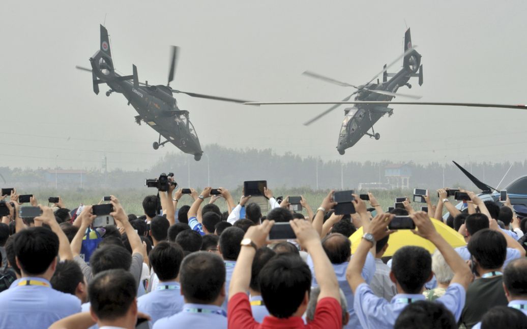Зрители фотографируют на телефоны маневры вертолетов во время выставки военной техники в Китае / © Reuters