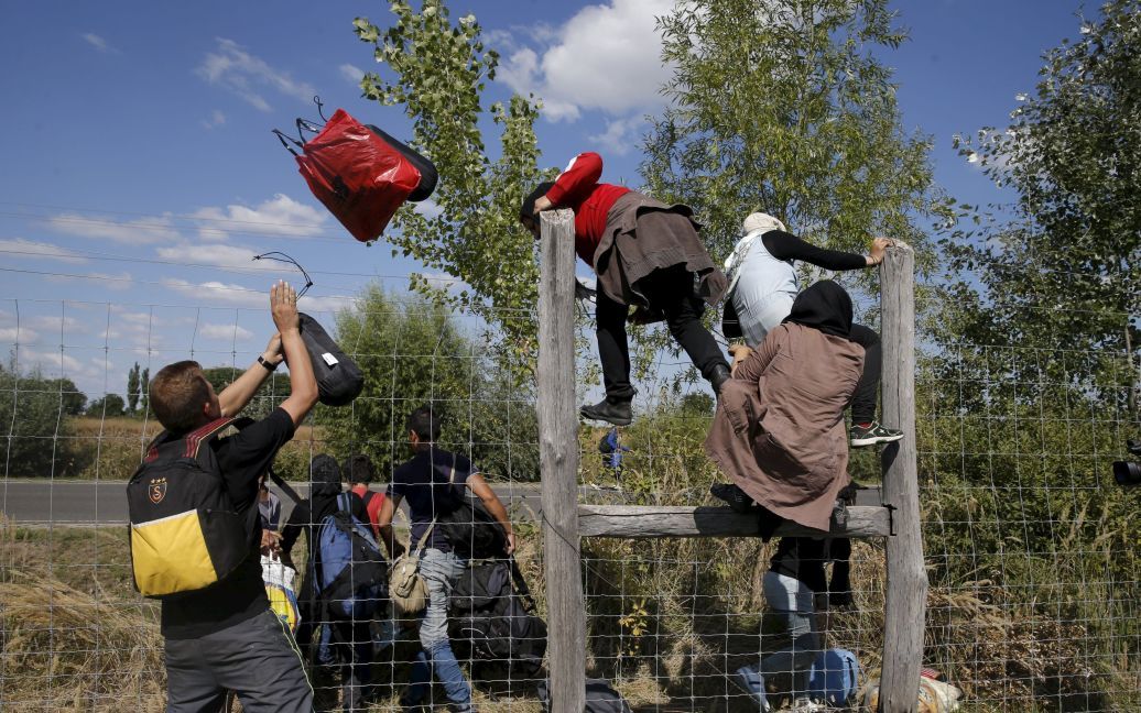 Мигранты перепрыгивают через забор, убегая из лагеря беженцев в Венгрии. С начала года в Европу приехали 365 тысяч беженцев, большинство которых &ndash; из Сирии, где продолжается война / © Reuters