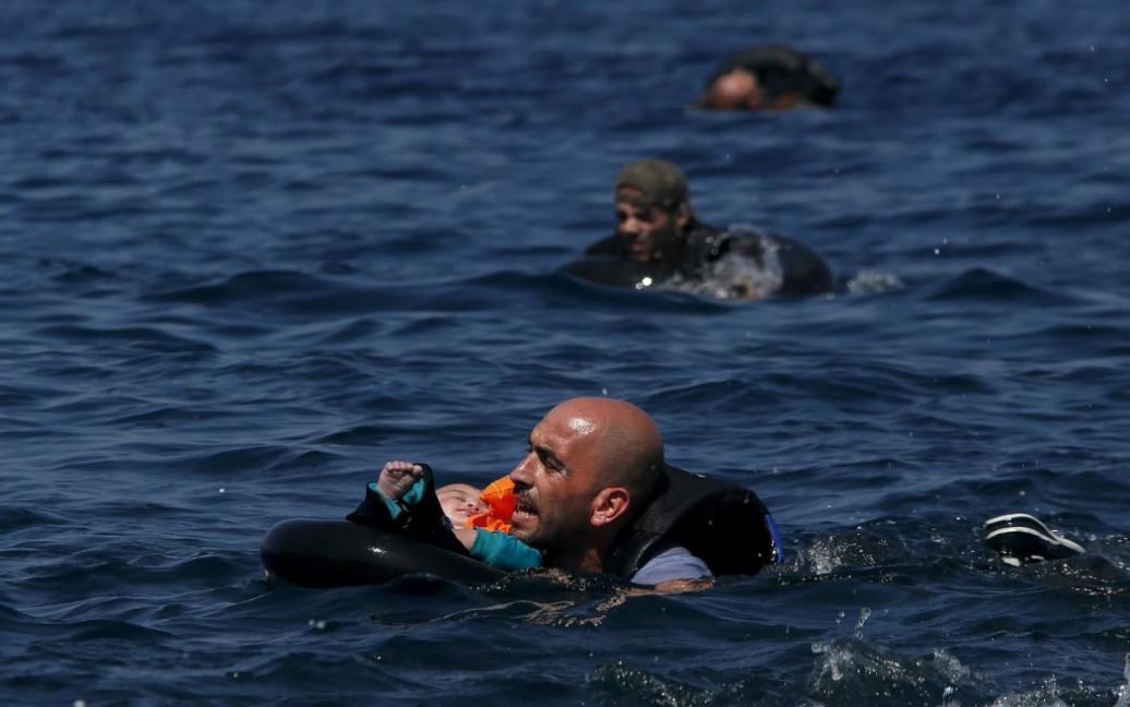 Сирийский беженец держит ребенка в спасательном жилете после того, как их лодка перевернулась в 100 метрах от греческого острова Лесбос. В общей сложности 432 тысячи беженцев и мигрантов прибегли к опасному путешествию через Средиземное море в Европу в этом году, по оценкам Международной организации по миграции. Около половины из них &mdash; сирийцы, которые бегут от гражданской войны. / © Reuters