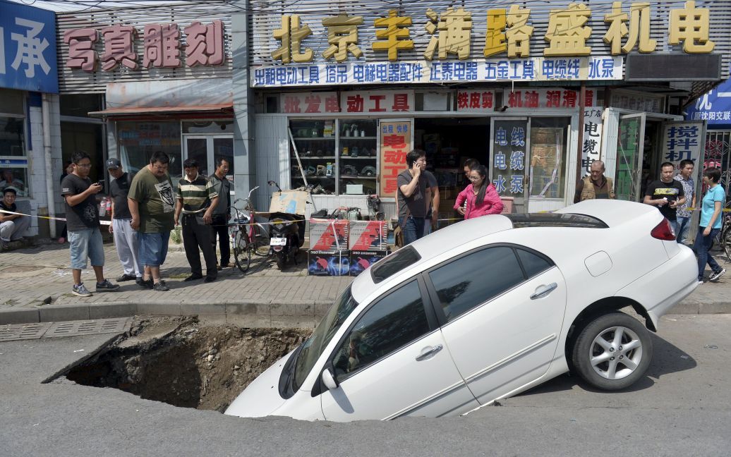 На улице в китайском Пекине автомобиль провалился в яму, которая внезапно возникла на дороге. Во время инцидента люди не пострадали / © Reuters