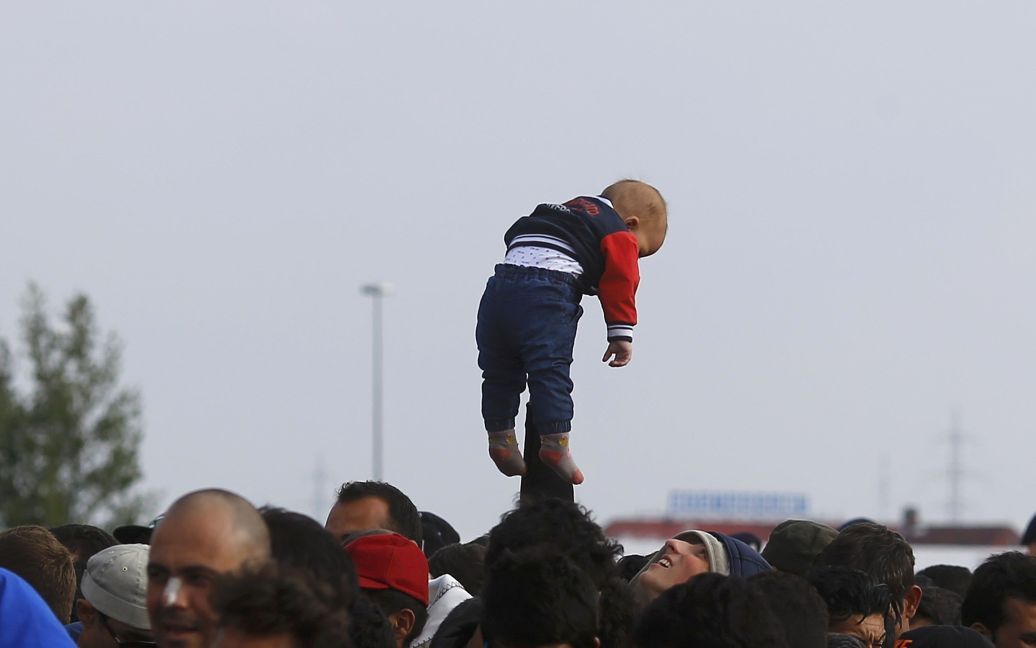 Мужчина держит ребенка над толпой в то время как мигранты ждут автобусы в точке пересечения границы между Венгрией и Австрией. Всего в ЕС сейчас находится около 160 тысяч беженцев, но в богатейшие страны Европы пытаются попасть еще сотни тысяч мигрантов. / © Reuters