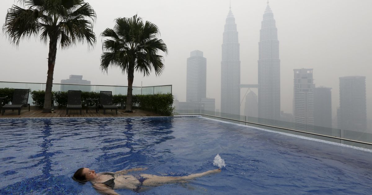 Женщина плавает в бассейне на крыше перед небоскребами Petronas Towers, окутанных смогом, в Куала-Лумпуре, Малайзия. Смог вызван лесными пожарами на индонезийских островах Суматра и Борнео, которые ухудшили качество воздуха в соседних Малайзии и Сингапуре. / © Reuters