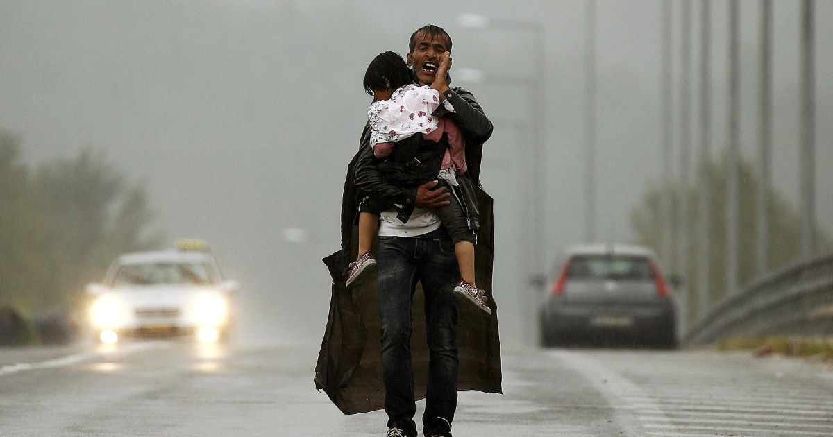 Сирійський біженець кричить до інших, щоб чекали на нього, доки він під дощем несе свого сина до кордону Греції з Македонією, недалеко від грецького села Ідоменей. Більшість біженців, які тікають в Європу від насильства та переслідування в Сирії, мають законне право на притулок, йдеться у заяві Організації Об'єднаних Націй. / © Reuters
